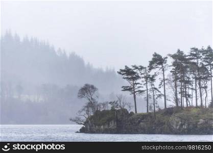 Beautiful calm peaceful Winter landscape over Thirlmere in Lake District with fog and layers of trees visible in the distance