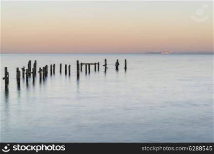 Beautiful calming long exposure landscape of ruined pier at sunset