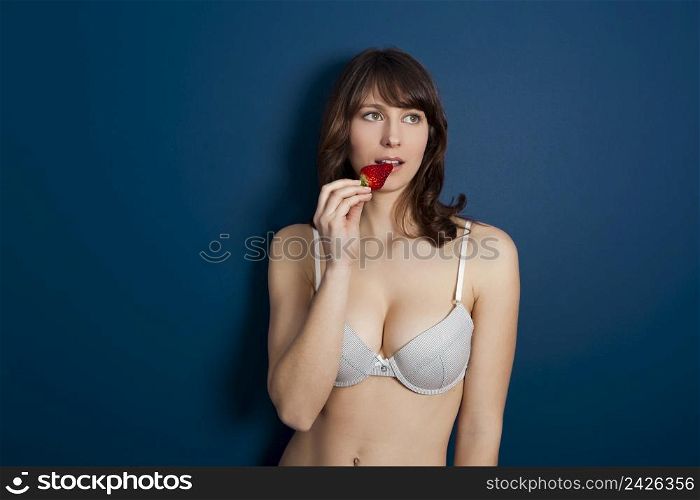 Beautiful casual young woman at home against a blue wall and eating strawberries
