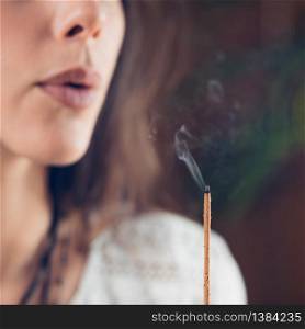 Beautiful Caucasian girl blowing smoke from burned incense stick.