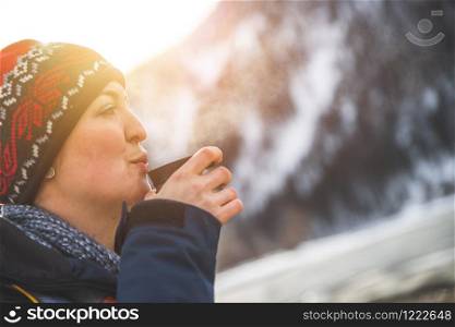 Beautiful Caucasian girl is holding a cup of tea outdoors, winter time