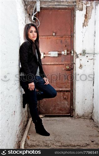 Beautiful Caucasian girl standing in basement in front of brown door leaning against white walls