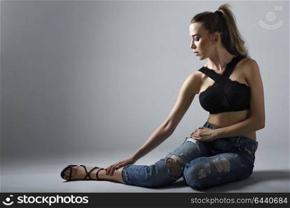 Beautiful caucasian woman with very long hair wearing black bra and blue jeans sitting on white floor. Wavy hairstyle. Studio shot.