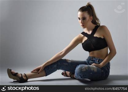 Beautiful caucasian woman with very long hair wearing black bra and blue jeans sitting on white floor. Wavy hairstyle. Studio shot.