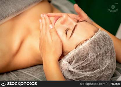 Beautiful caucasian young woman receiving a facial massage with closed eyes in spa salon, close up. Relaxing treatment concept. Beautiful caucasian young woman receiving a facial massage with closed eyes in spa salon, close up. Relaxing treatment concept.