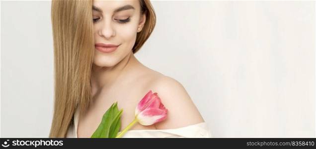 Beautiful caucasian young woman with one tulip looking on a flower against a white background. Young woman with one tulip