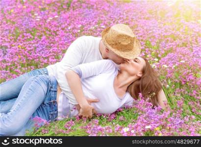 Beautiful cheerful couple lying down on floral glade and kissing, romantic date in spring park, young family, love and romance concept