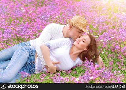 Beautiful cheerful couple lying down on floral glade and kissing, romantic date in spring park, young family, love and romance concept&#xA;