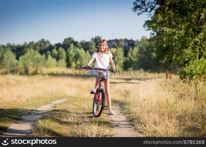 Beautiful cheerful girl riding bike in meadow at sunny day