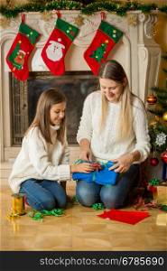 Beautiful cheerful mother and daughter wrapping Christmas presents on floor at fireplace