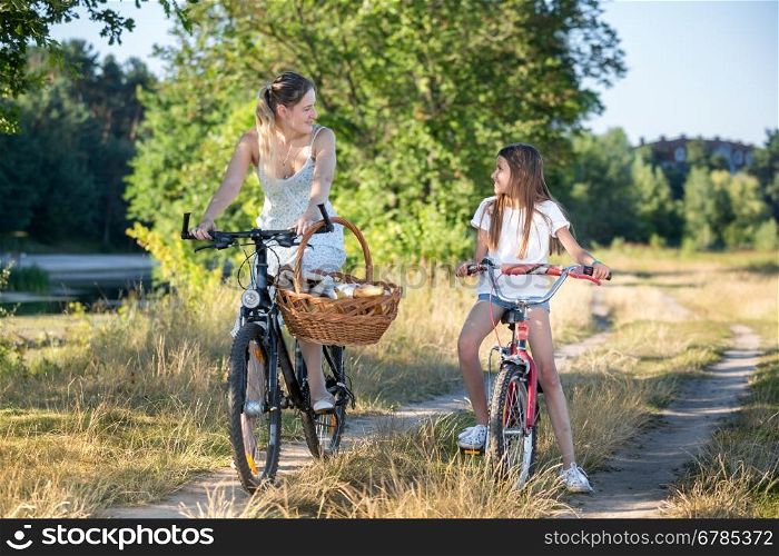 Beautiful cheerful mother going to picnic with daughter on bicycles