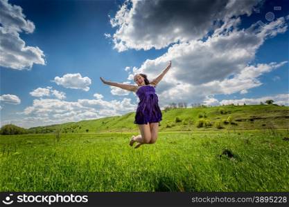 Beautiful cheerful woman jumping up high in the meadow with fresh green grass
