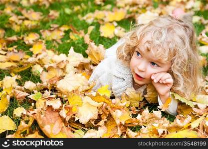 Beautiful child lying on yellow maple leaves in autumn park