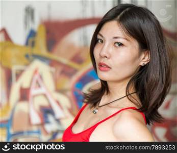 Beautiful Chinese woman by graffiti walls, looking at camera