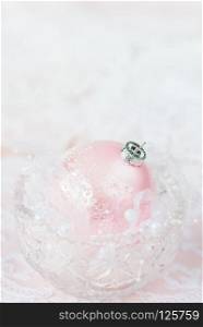 Beautiful Christmas decoration: a large pink Christmas ball with a white ribbon and pearls in a crystal vase on a light background, with copy-space