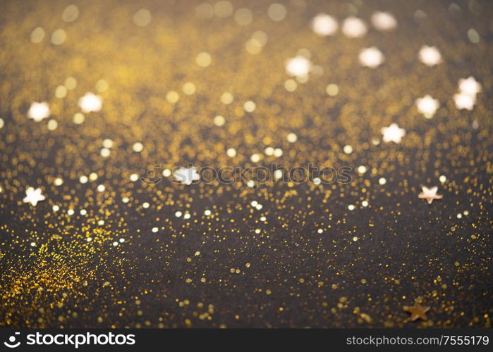 Beautiful Christmas light and stars background. Abstract glitter bokeh and scattered sparkles in gold, on black. Beautiful Christmas light background