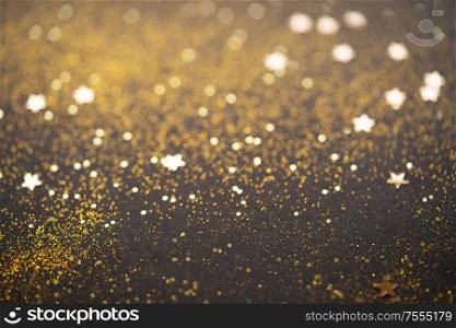 Beautiful Christmas light and stars background. Abstract glitter bokeh and scattered sparkles in gold, on black. Beautiful Christmas light background