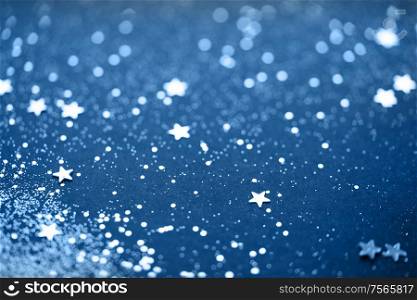 Beautiful Christmas light background. Abstract glitter bokeh and scattered sparkles in classic blue color, on black. Beautiful Christmas light background.