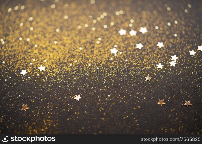 Beautiful Christmas light background. Abstract glitter bokeh and scattered sparkles in gold, on black. Beautiful Christmas light background.