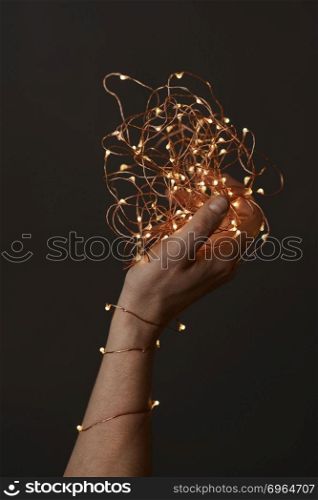 beautiful christmas lights garland in a female hand on a dark background. bright christmas lights in woman&rsquo;s hands