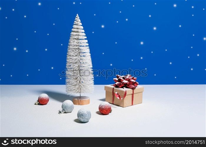 Beautiful Christmas or New Year banner with copy space. Toy Christmas tree, gift box with red bow and Christmas baubles on blue background with snow falling on the background. Beautiful Christmas or New Year banner with copy space. Toy Christmas tree, gift box with red bow and Christmas baubles on blue background with snow falling on the background.