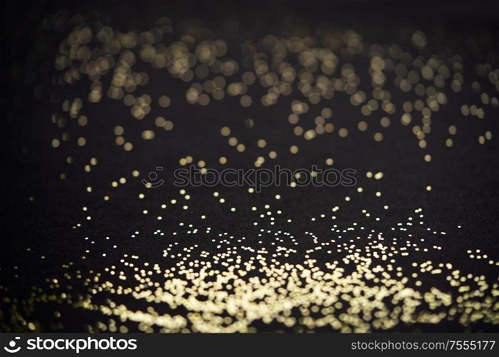Beautiful Christmas shimmering light background. Abstract glitter bokeh and scattered sparkles in gold, on black. Beautiful Christmas light background. Abstract glitter bokeh and scattered sparkles in gold, on black