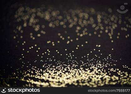 Beautiful Christmas shimmering light background. Abstract glitter bokeh and scattered sparkles in gold, on black. Beautiful Christmas light background. Abstract glitter bokeh and scattered sparkles in gold, on black