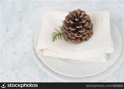 Beautiful Christmas table: pine cone lies on beautiful white porcelain plate with a linen napkin, which is located on a light table