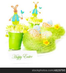 Beautiful colorful chicken eggs in the nest decorated with flowers and pretty rabbit toys isolated on white background, festive Easter postcard