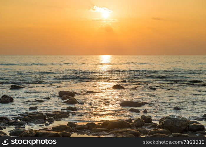 Beautiful colorful sunset landscape with sand beach, golden sun and stones at sea shore