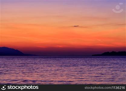 Beautiful, colorful sunset on the sea, mountains silhouettes and bright traces of tracks of flying planes in the sky, image with copy space.. Beautiful, bright sunset on the Gulf of Corinth against the background of the silhouette of the highlands running along the horizon of the sea line.