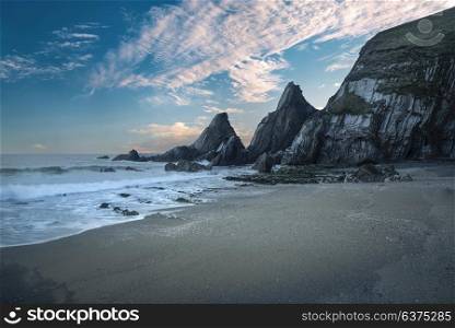 Beautiful colorful sunset over beach landscape with jagged rock formations