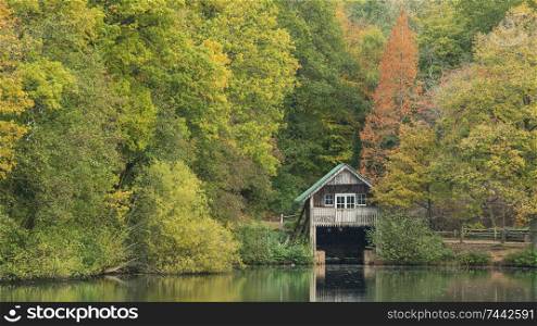 Beautiful colorful vibrant Autumn Fall landscape image of boathouse on lake in forest scene
