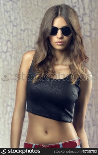 Beautiful, confident, young woman with sunglasses. She wear black top, jeans. She is showing her belly.