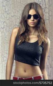 Beautiful, confident, young woman with sunglasses. She wear black top, jeans. She is showing her belly.