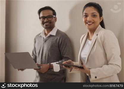 Beautiful corporate couple looking at camera while doing office work using laptop and digital tablet