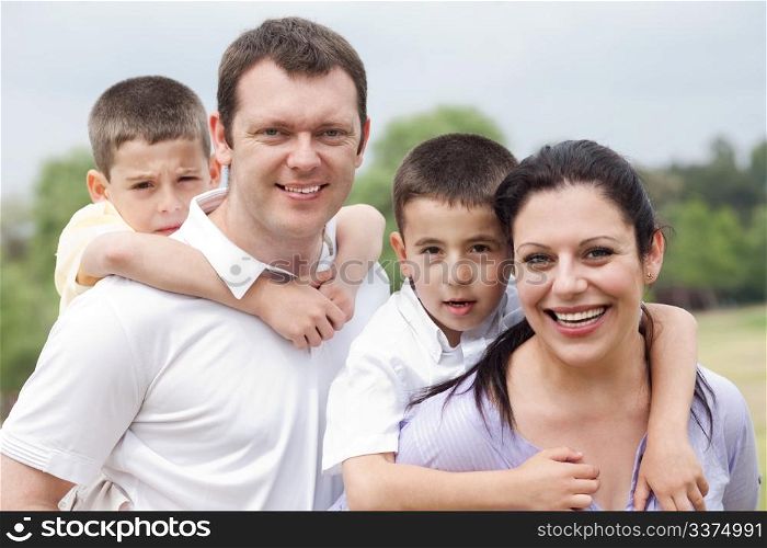 Beautiful couple carrying their kids on their back and looking at camera on natural background