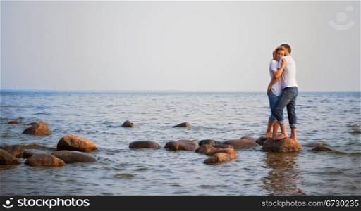 beautiful couple embrace on a stone in sea