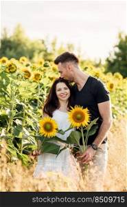Beautiful couple having fun in sunflowers field. A man and a woman in love walk in a field with sunflowers, a man hugs a woman. selective focus.. Beautiful couple having fun in sunflowers field. A man and a woman in love walk in a field with sunflowers, a man hugs a woman. selective focus