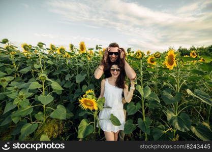 Beautiful couple in sunglases having fun in sunflowers field. A man and a woman in love walk in a field with sunflowers, a man hugs a woman. selective focus.. Beautiful couple in sunglases having fun in sunflowers field. A man and a woman in love walk in a field with sunflowers, a man hugs a woman. selective focus