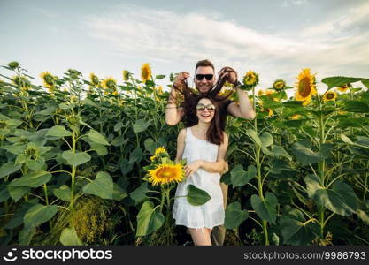 Beautiful couple in sunglases having fun in sunflowers field. A man and a woman in love walk in a field with sunflowers, a man hugs a woman. selective focus.. Beautiful couple in sunglases having fun in sunflowers field. A man and a woman in love walk in a field with sunflowers, a man hugs a woman. selective focus