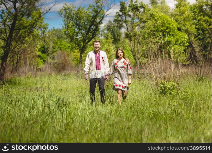 Beautiful couple in traditional slavic clothes walking at meadow