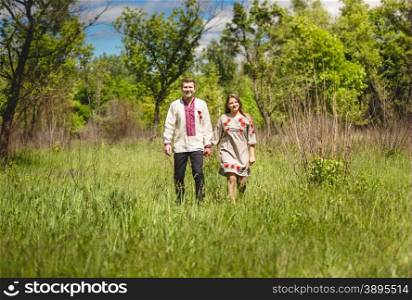 Beautiful couple in traditional slavic clothes walking at meadow