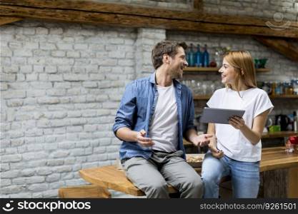 Beautiful couple is using a digital tablet and smiling while sitting on the table at home