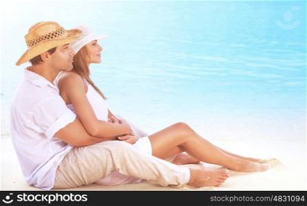 Beautiful couple on the beach, sitting on the coast and hugging, enjoying peaceful sunny day on tropical resort, romantic summer vacation