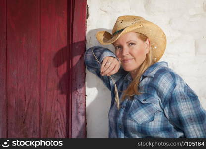 Beautiful Cowgirl Wearing Cowboy Hat Leaning Against Old Adobe Wall and Red Door.