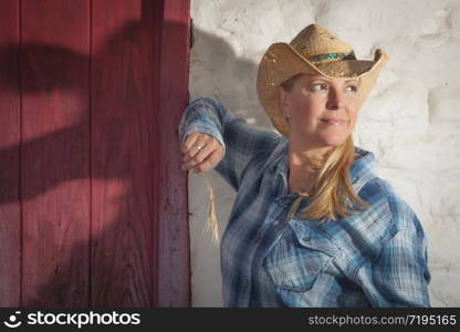 Beautiful Cowgirl Wearing Cowboy Hat Leaning Against Old Adobe Wall and Red Door.