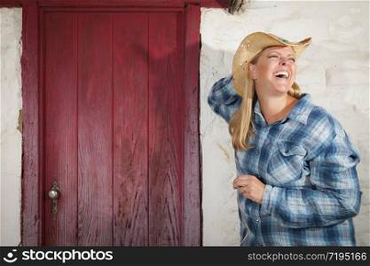 Beautiful Cowgirl Wearing Cowboy Hat Leaning Against Old Adobe Wall and Red Door.