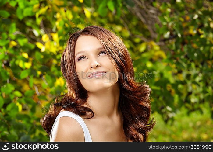 Beautiful curly smiling girl against green foliage