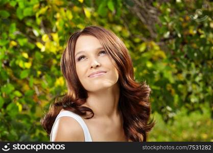 Beautiful curly smiling girl against green foliage